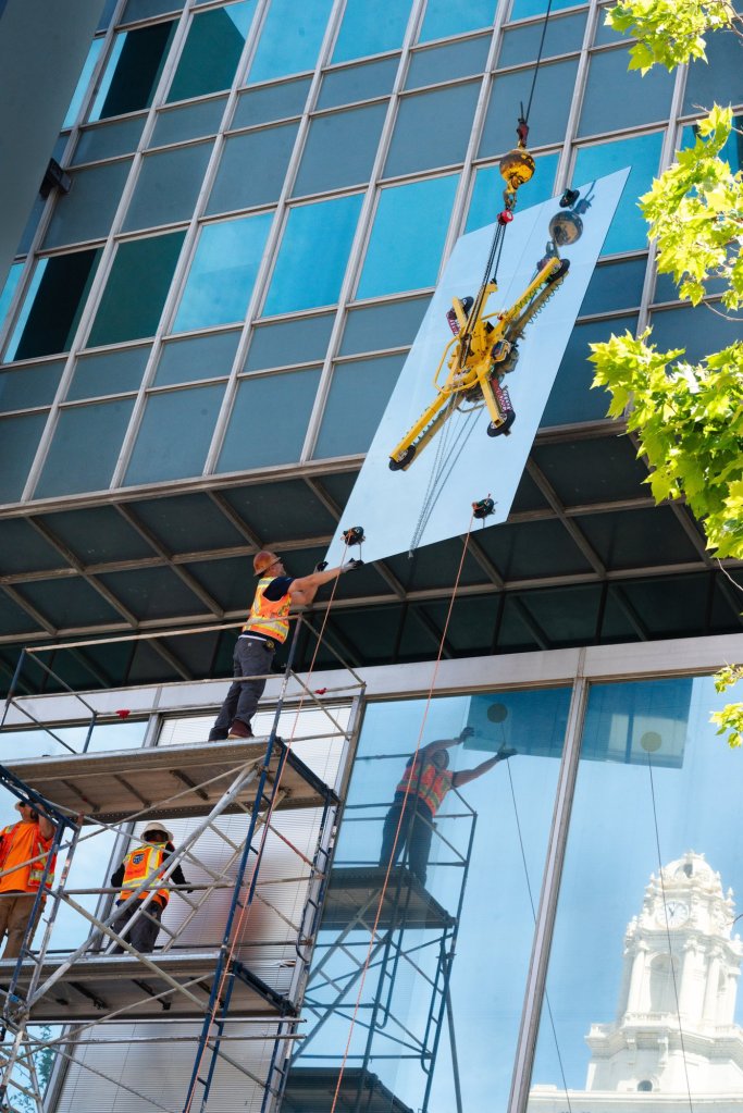 East Bay Glass crew guiding a large glass panel set by crane with a vacuum lifter on Broadway in downtown Oakland