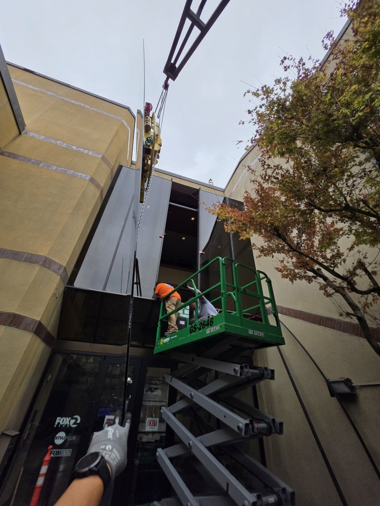 Tall atrium glass panel lifted with a quad-cup vacuum lifter and scissor lift at the KTVU Fox 2 building in Oakland
