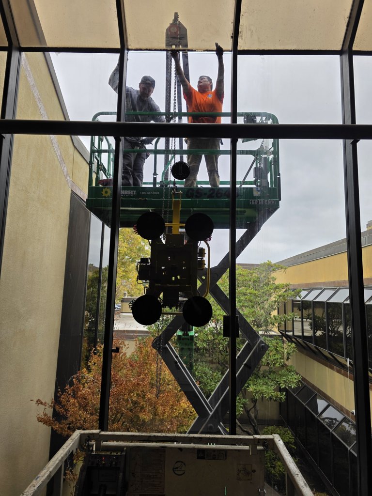 East Bay Glass glaziers on a scissor lift setting tall atrium glass with a vacuum lifter at the KTVU Fox 2 building in Oakland